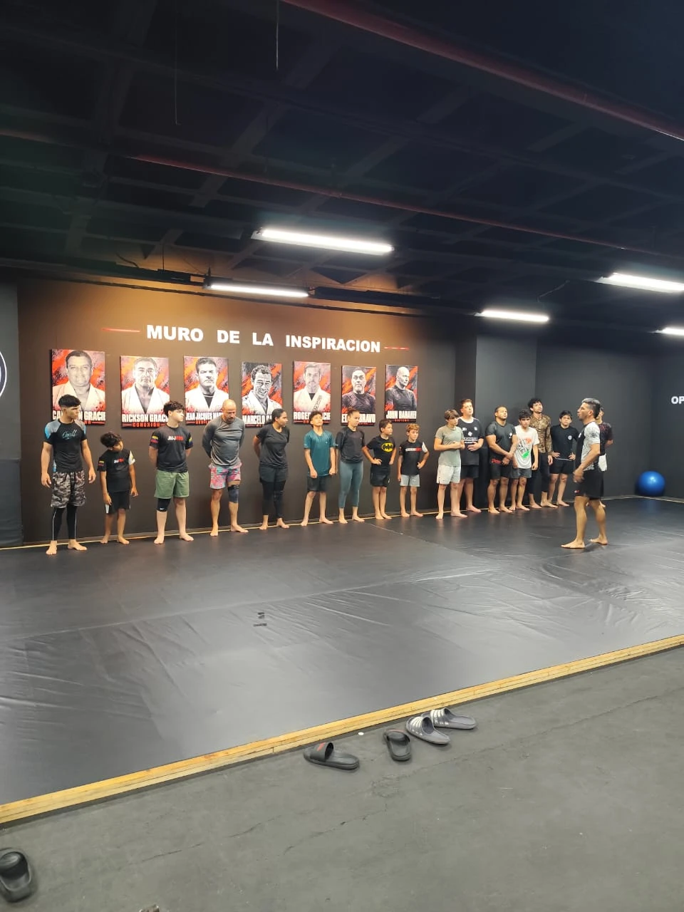 Alumnos en fila sobre el tatami, de espaldas al Muro de la inspiración, escuchando al profesor